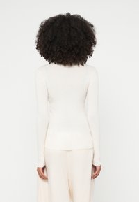 Camisola comprida de manga comprida canelada em creme, com um design ajustado, decote redondo e textura suave. Vista por trás.