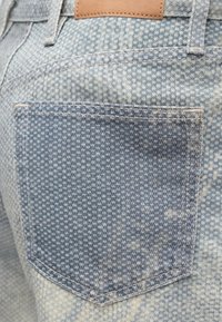 Lys blå denimstoff med en sydd baklomme, med et teksturert mønster og et lite brunt lærmerke over linningen.