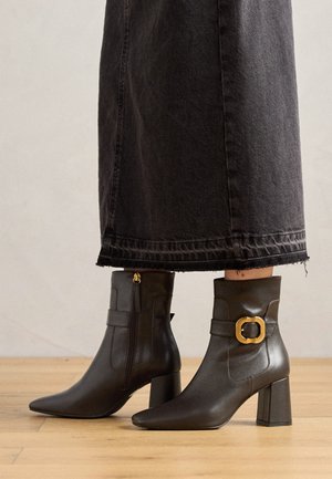 Black leather ankle boots with a pointed toe, featuring a gold buckle accent and a block heel. Smooth texture and zip closure on the side.