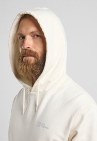 Weißer Kapuzenpullover mit verstellbaren Kordeln und strukturiertem Finish. Verfügt über ein kleines, dezentes Logo auf der linken Brust.