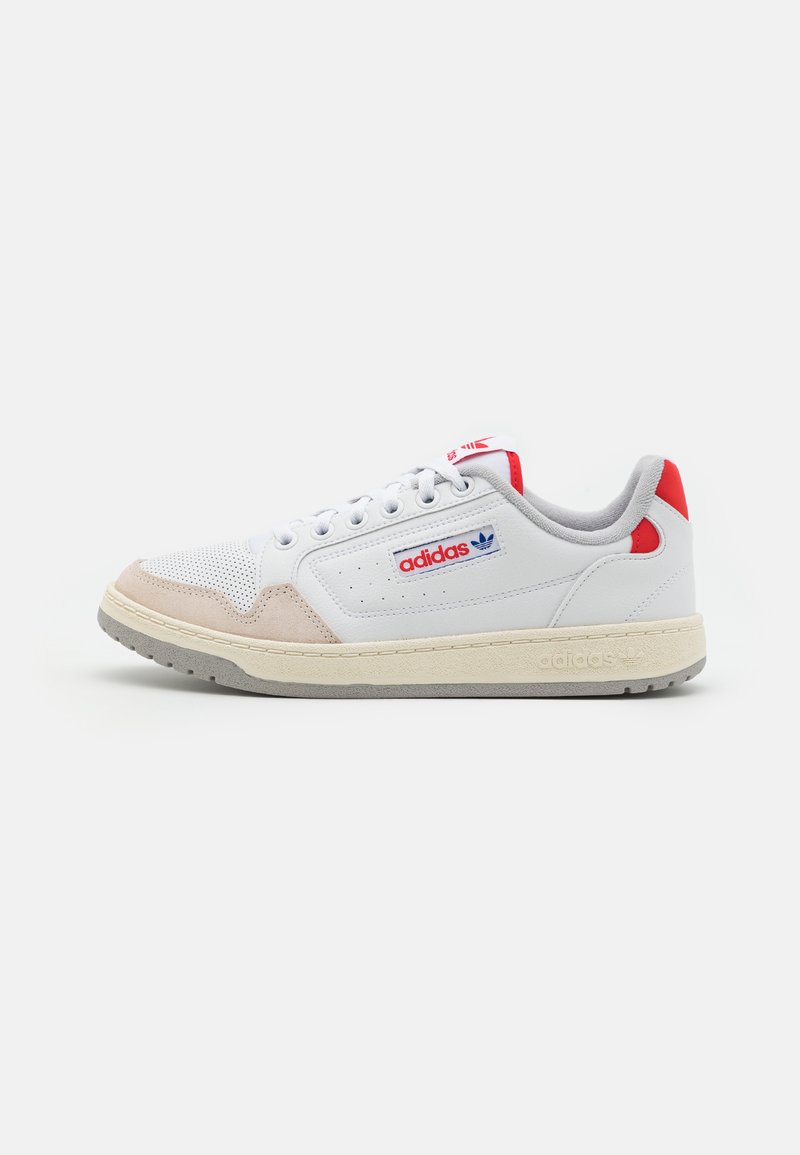 Zapatilla blanca y beige con acentos grises, diseño de piel perforada y detalles rojos. Cuenta con una suela texturizada y un logo en navy.