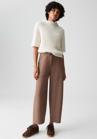 Crème, textuur short-sleeve trui, gecombineerd met hoge taille, wijde bruine broeken met voorzakken en een knoopsluiting. Bruine sneakers.