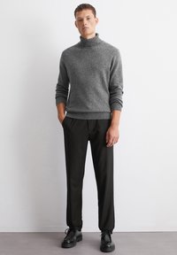 Maglione grigio a collo alto in maglia con polsini a coste abbinato a pantaloni slim-fit neri a righe sottili e scarpe nere stringate. Design semplice e pulito.
