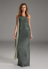 Abendkleid mit einem Schulterträger in dunkelgrün mit Pailletten. Verfügt über einen fließenden, hellgrünen Schal, der über eine Schulter drapiert ist. Glatte, figurbetonte Silhouette.