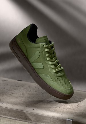 Sneaker verde in suede con un design testurizzato, caratterizzato da una punta perforata, lacci coordinati e una suola in gomma marrone. Logo impresso sul lato.
