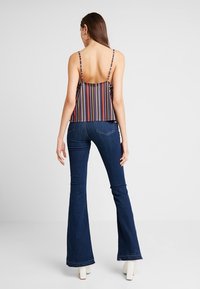 Top con spalline e strisce verticali multicolori, abbinato a jeans a zampa blu. Tessuto morbido, design con schiena scoperta, estetica casual.