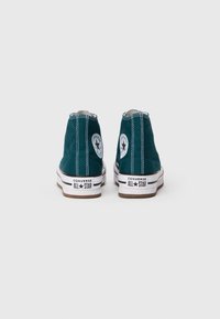 Zelene visoke Converse All Star superge gledane s hrbtne strani na enobarvni beli podlagi.