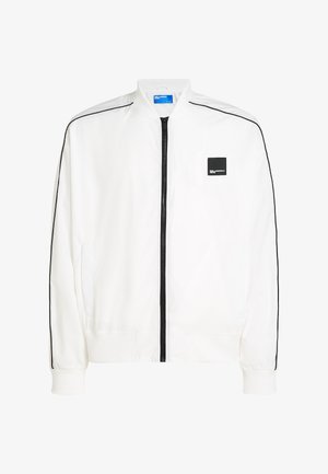 Balta bomber stila jaka ar priekšējo rāvējslēdzēju, melnām sānu svītrām, elastīgiem aprocēm un nelielu melnu logotipa ielāpu uz kreisā krūšu rajona.