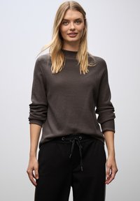 Maglione grigio testurizzato con maniche lunghe, colletto a costine, indossato sopra pantaloni jogger neri con coulisse. Design semplice, vestibilità casual.