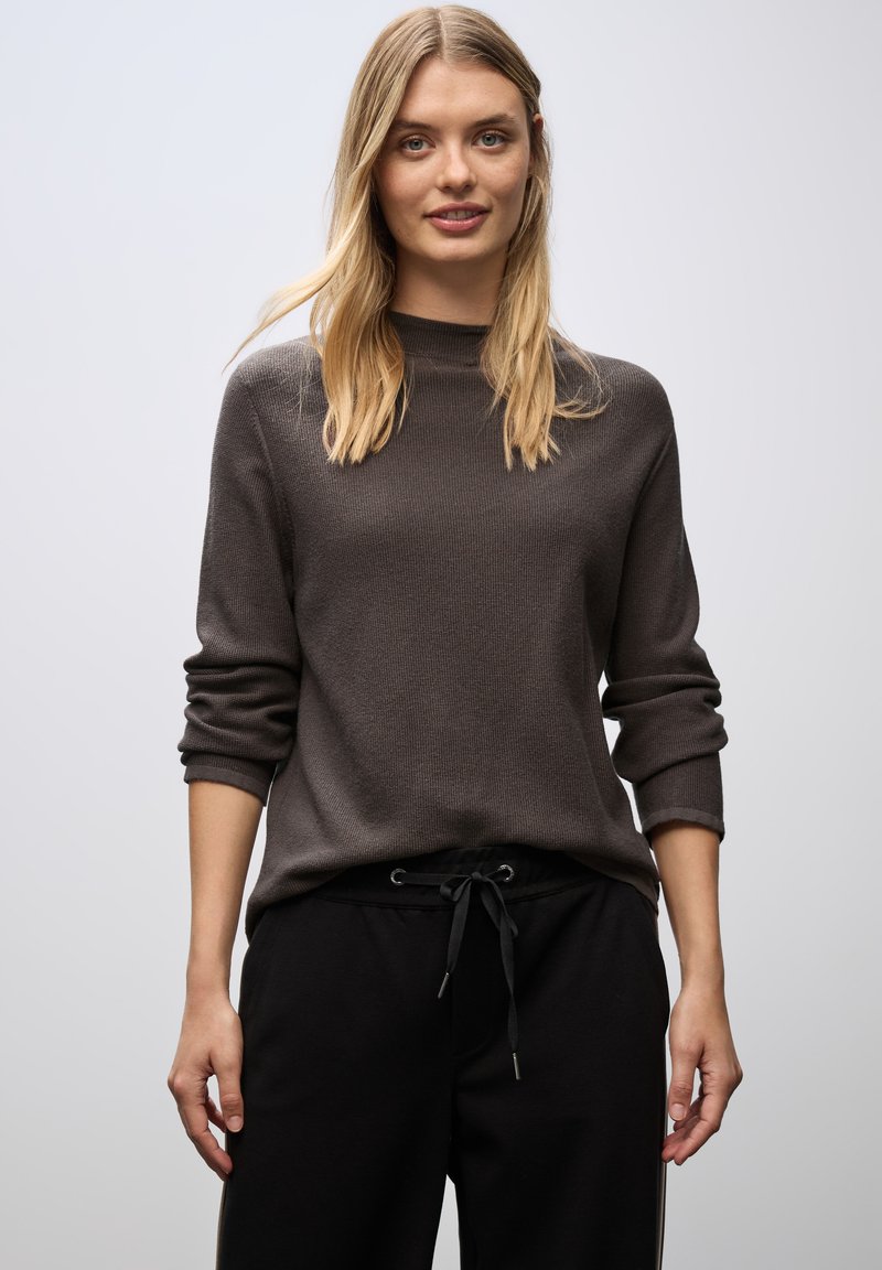 Maglione grigio testurizzato con maniche lunghe, colletto a costine, indossato sopra pantaloni jogger neri con coulisse. Design semplice, vestibilità casual.