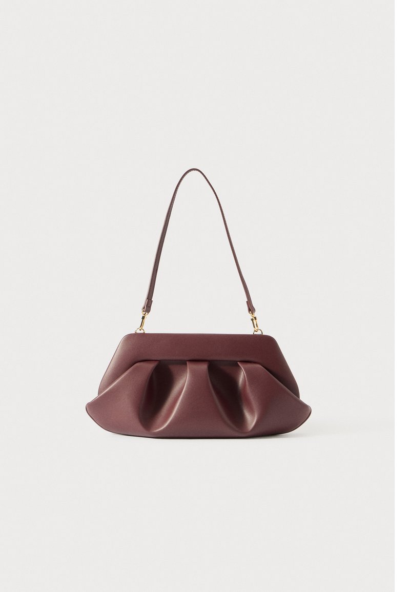 Μαλακή μπορντώ δερμάτινη τσάντα με δομημένες πτυχές και μία μόνο λωρίδα που ασφαλίζεται με χρυσές αγκράφες σε απλή λευκή φόντο.