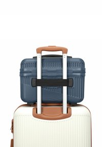 Due valigie impilate; quella superiore è blu navy con una superficie texture e cinture nere, mentre quella inferiore è bianca con linee rigate e una maniglia marrone.