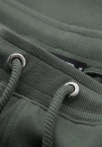 Close-up of green ribbed fabric waistband with thick drawstrings threaded through silver metal eyelets.
