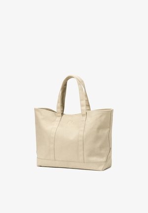 Beige canvas tote bag with two handles and subtle stitched logo on front, standing upright on a white background.