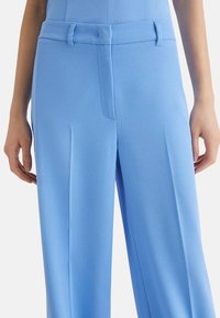 Pantaloni su misura blu chiaro realizzati in un tessuto morbido, con fronte piatto, pieghe sottili e una vita con passanti per la cintura.