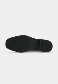 Semelle de chaussure habillée noire avec des motifs géométriques sur la bande de roulement et le nom de la marque "GANT" embossé près de la zone de la voûte plantaire.