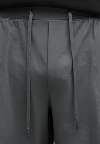 Des shorts de sport gris sont présentés, avec une taille à cordon de serrage et des embouts noirs, affichés de la taille vers le bas sur un fond neutre.