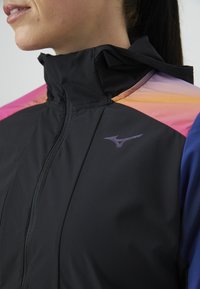 Fekete sportdzseki cipzárral és magas gallérral. Színes, rózsaszín és narancssárga színátmenetek díszítik a vállakat. Puha tapintású.