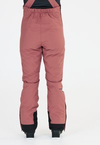 Rosa Schneehosen mit verstellbaren Trägern, die einen lockeren Schnitt, ein elastisches Bündchen und schwarze Knöchelriemen mit Reißverschlüssen aufweisen.