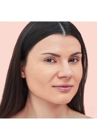 Primo piano di una persona con capelli lunghi, lisci e scuri e una pelle liscia, su uno sfondo rosa chiaro. Trucco naturale, toni neutri.