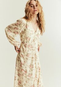 Blommig klänning i mjuk gul tyg med ros mönster i rosa och grönt, långa puffärmar, V-ringning och rynkad midjedetalj.