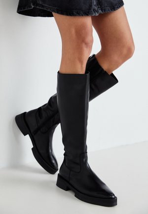 Czarne skórzane buty za kolano z szpiczastym noskiem, płaską podeszwą i minimalnym szwem. Gładka tekstura i prosty design bez ozdób.