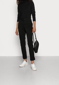 Černý rolákový svetr, černé úzké kalhoty, bílé tenisky a malá černá crossbody taška. Jednoduchý, současný design s minimálními doplňky.