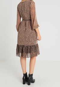 Robe à imprimé léopard avec manches trois-quarts, taille cintrée et ourlet à volants à plusieurs niveaux, en tissu léger et semi-transparent ; bottines noires.