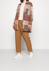 Rutig flanellskjorta i röd, brun och grå, över en ljusrosa topp. Bruna smala byxor och vita sneakers fulländar outfiten.