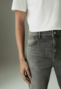 Grijze denim jeans met een slim fit, voorzien van oranje stiksels, een voorzak en een knoopsluiting in de taille. Gepaard met een wit T-shirt.