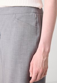 Grijze op maat gemaakte broeken van een gestructureerde stof, met een schuine voorkantzak en een subtiele merkdetail op de tailleband.