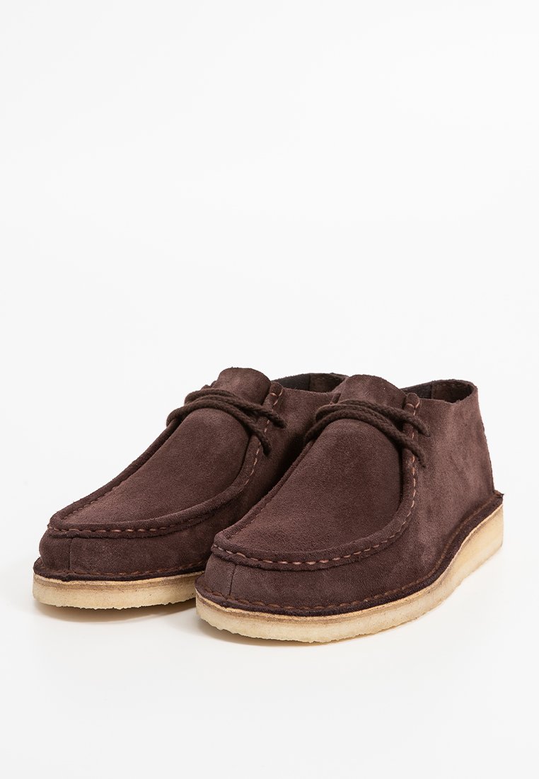 Braune Wildleder-Loafers mit gesteppten Details, runder Zehenpartie und Schnürverschluss. Weiches Material, flache Gummisohle und minimalistisches Design.