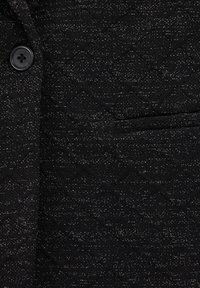 Svart texturerad tyg med subtila metalltrådar. Inkluderar en svart knapp och en ficka med slät yta. Designen visar ett vågformigt mönster.