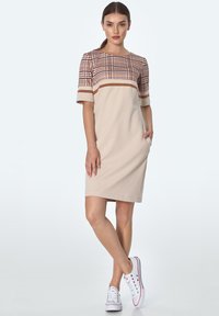 Beżowa sukienka do kolan z górą w kratę i paskowanymi akcentami. Posiada krótkie rękawy oraz dwie boczne kieszenie, zestawiona z białymi trampkami.