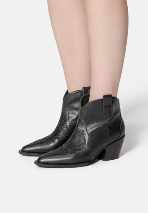 Bottines en cuir noir avec des bouts pointus, motif floral brodé sur les côtés et un talon carré bas. Texture lisse, design minimaliste.