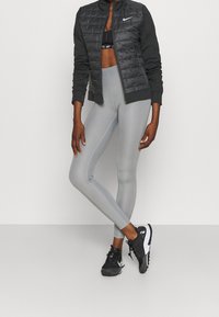 Chaqueta negra acolchada con mangas grises, leggings grises de cintura alta y zapatillas deportivas negras. Diseño simple y moderno con una silueta ajustada.