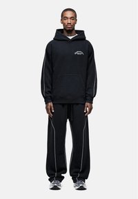 Zwarte hoodie met een voorzak en klein logo, gecombineerd met bijpassende losvallende broek met witte stiksels.