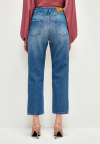 Jeans de mezclilla azul con cintura alta, diseño de pierna recta y lavado desgastado. Presenta dos bolsillos traseros y una etiqueta de cuero marrón en la cintura.