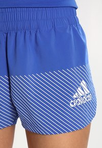 Blå idrottsshorts har ett diagonalt mönster av vita ränder och ett elastiskt midjeband, med en prägling av en logotyp på nedre delen.