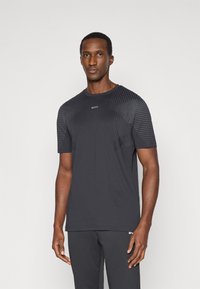 Μαύρο αθλητικό μπλουζάκι με ραγλανά μανίκια, διαθέτει υφασμάτινες οριζόντιες ρίγες στους ώμους. Το λογότυπο είναι τοποθετημένο στο κέντρο του στήθους.