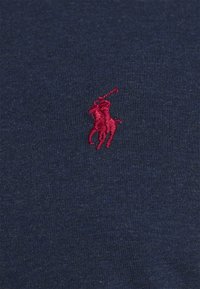 Mörkblå T-shirt i tyg med texturerad ribb, med en liten, broderad röd polo-spelare logotyp på vänster bröstområde.
