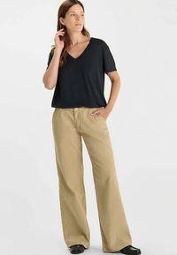 Zwart V-hals T-shirt gecombineerd met beige wijde pijpen broek. De broek heeft een relaxte pasvorm en zakken; het T-shirt heeft korte mouwen en een losse snit.