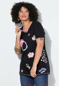 Camiseta negra con varios estampados coloridos, incluidos eslóganes y símbolos. Mangas cortas, cuello redondo y acabada con un ribete en contraste.