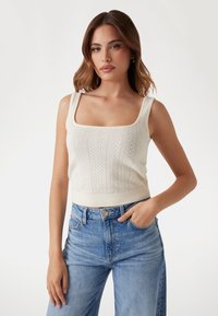 Creme, strikket crop top med firkantet halsudskæring og struktureret mønster. Parret med højtaljede blå denimjeans.