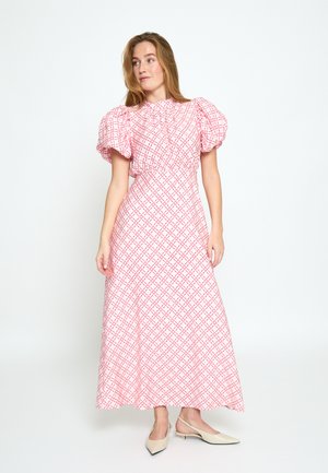 Frau trägt ein rosa-weiß kariertes Maxikleid mit kurzen Puffärmeln und beige Slingback-Pumps, steht vor einem schlichten Hintergrund.