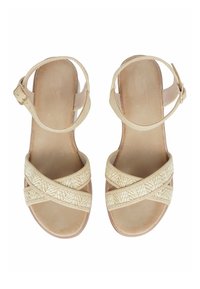 Sandali beige con un design a strap incrociato realizzati in materiale intrecciato. Presentano una cinghia alla caviglia con fibbia e una suola piatta. Texture liscia.