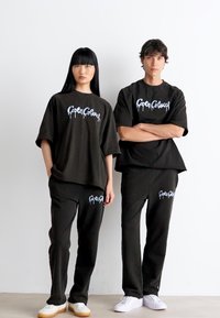 Zwarte oversized t-shirts en bijpassende sweatpants met blauwe graffiti-achtige tekst. Gemaakt van zachte stof met een relaxte pasvorm.