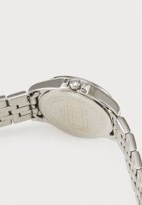 Silver wristwatch with a stainless steel band, rounded case, and a visible crown. The back has engraved branding and certification details.