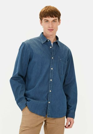 Mørkeblå denim skjorte med knapper, brystlomme, lange ærmer og klassisk krave. Har et diskret mønster og hvide knapper.