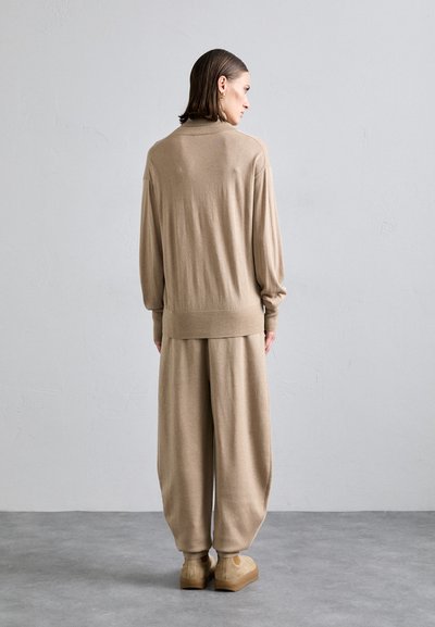 Beige knit sweater with long sleeves and ribbed hem, paired with loose-fitting beige trousers. Features smooth texture and relaxed silhouette.